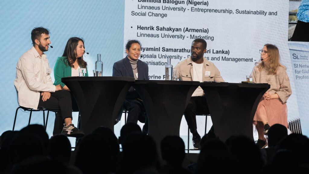 A panel of 4 young speakers and a moderator sat at a table on stage in front of a big screen with slides